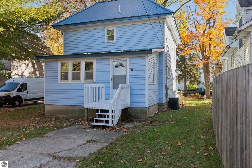 Gorgeous renovated blue home with white trim and steps, featuring new siding and a metal roof, located at 117 E Wright Avenue, Shepherd, MI, surrounded by autumn foliage and nearby vehicles.