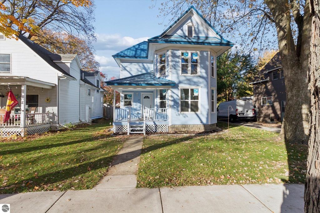 Renovated two-story home at 117 E Wright Avenue, Shepherd, MI, featuring a blue roof, large windows, and a porch, surrounded by green lawn and neighboring houses.