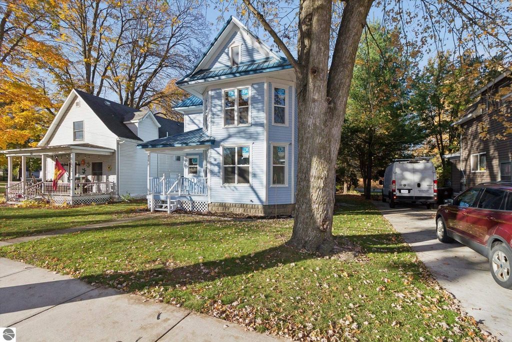 Renovated blue Victorian-style home at 117 E Wright Avenue, Shepherd, MI, featuring a large front porch, surrounded by autumn foliage and neighboring houses.