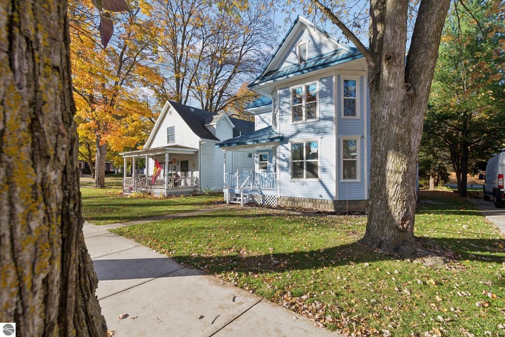 Renovated blue Victorian-style home at 117 E Wright Avenue, Shepherd, MI, featuring a welcoming porch, surrounded by autumn foliage, showcasing new windows and a metal roof.