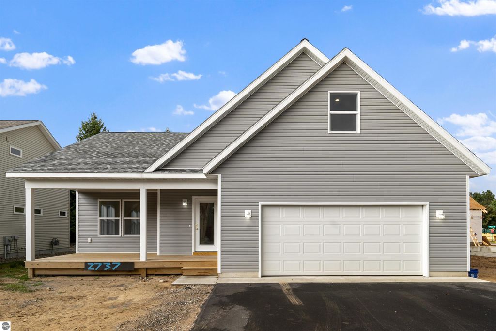 Newly constructed home at 2737 Ruby Street, Traverse City, featuring a modern exterior with gray siding, front porch, and attached garage, set against a clear blue sky.