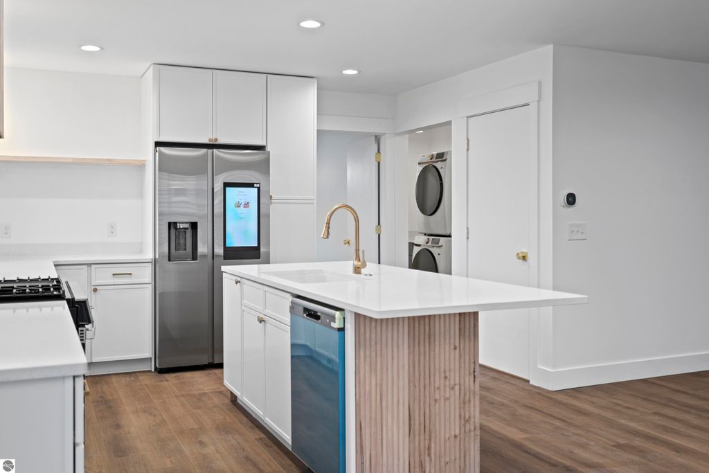 Modern kitchen featuring stainless steel appliances, quartz countertops, custom cabinetry, and a spacious island with a wood-accented base, showcasing a bright and open layout ideal for contemporary living.