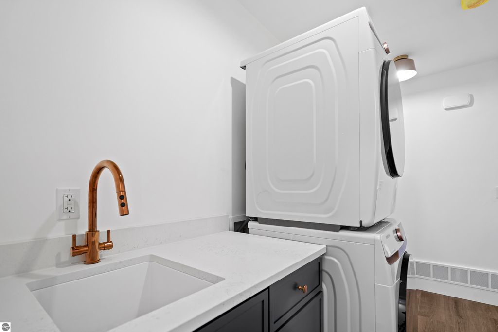 Modern laundry room featuring stacked white washer and dryer, sleek quartz countertop with a deep sink, and a stylish copper faucet, reflecting efficient design in the new Emerald Hills community home.