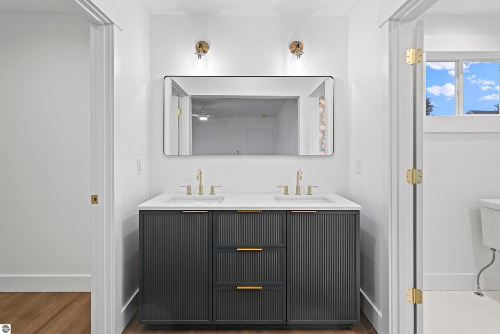 Modern bathroom featuring dual sinks, quartz countertop, stylish dark cabinetry, and a large mirror, showcasing quality finishes and craftsmanship in the new home at 2737 Ruby Street, Traverse City, MI.