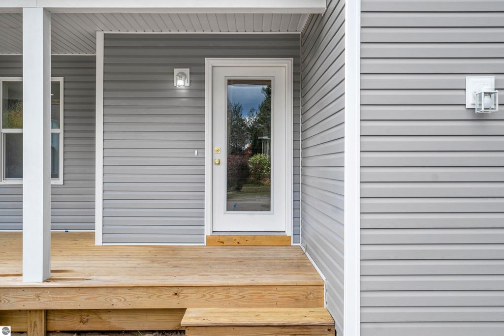 Front entryway of a modern home at 2737 Ruby Street, featuring gray siding, a white door with glass panel, and wooden porch steps, showcasing craftsmanship and design in the Emerald Hills community of Traverse City.