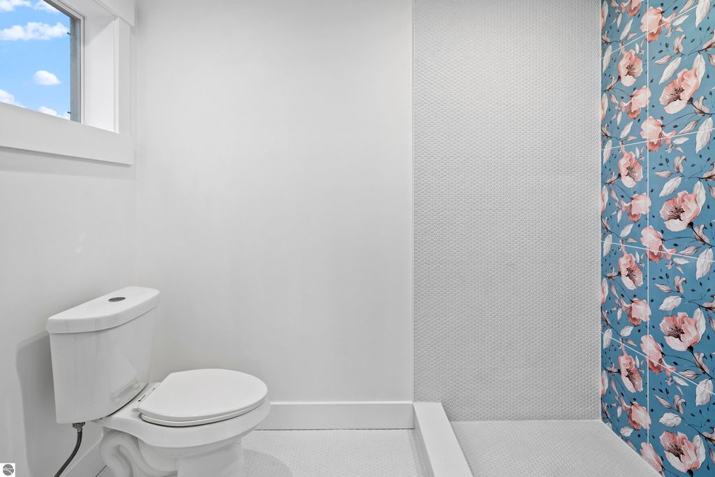 Modern bathroom featuring a white toilet, textured shower wall, and vibrant floral tile accent wall, highlighting craftsmanship and design in the new Emerald Hills community home in Traverse City.