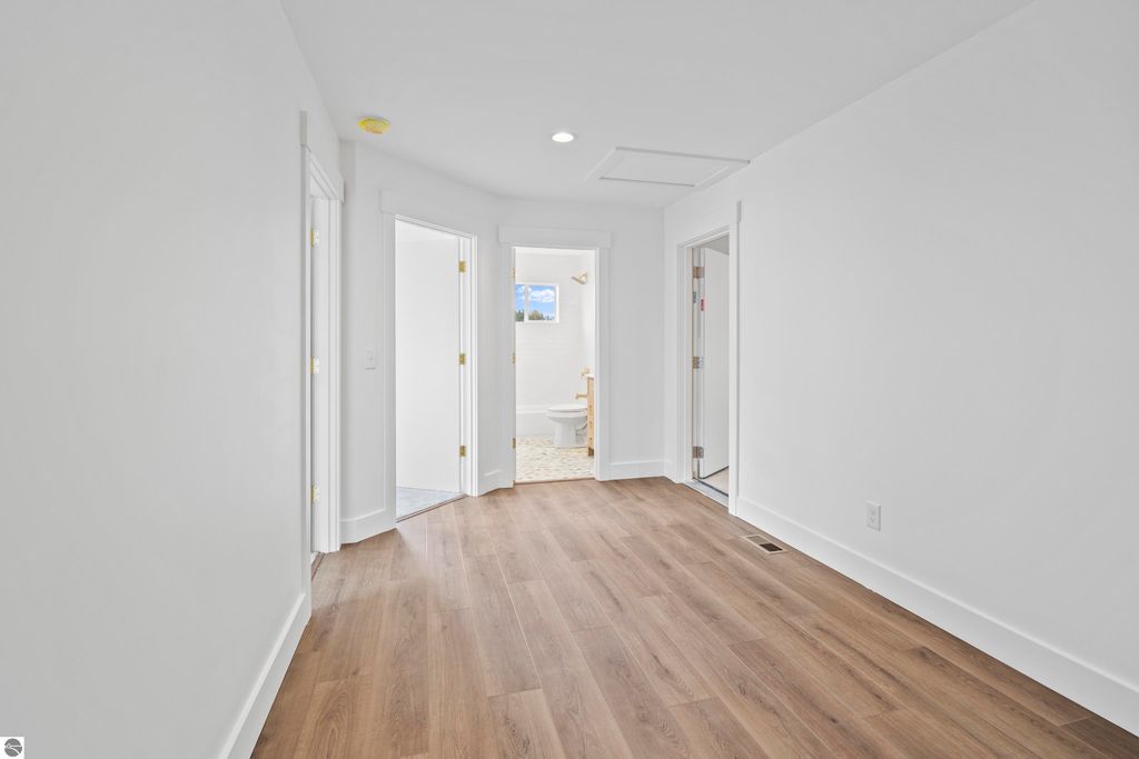 Bright, open hallway featuring modern design, hardwood flooring, and multiple doorways leading to rooms in a new home located in Emerald Hills, Traverse City, MI.