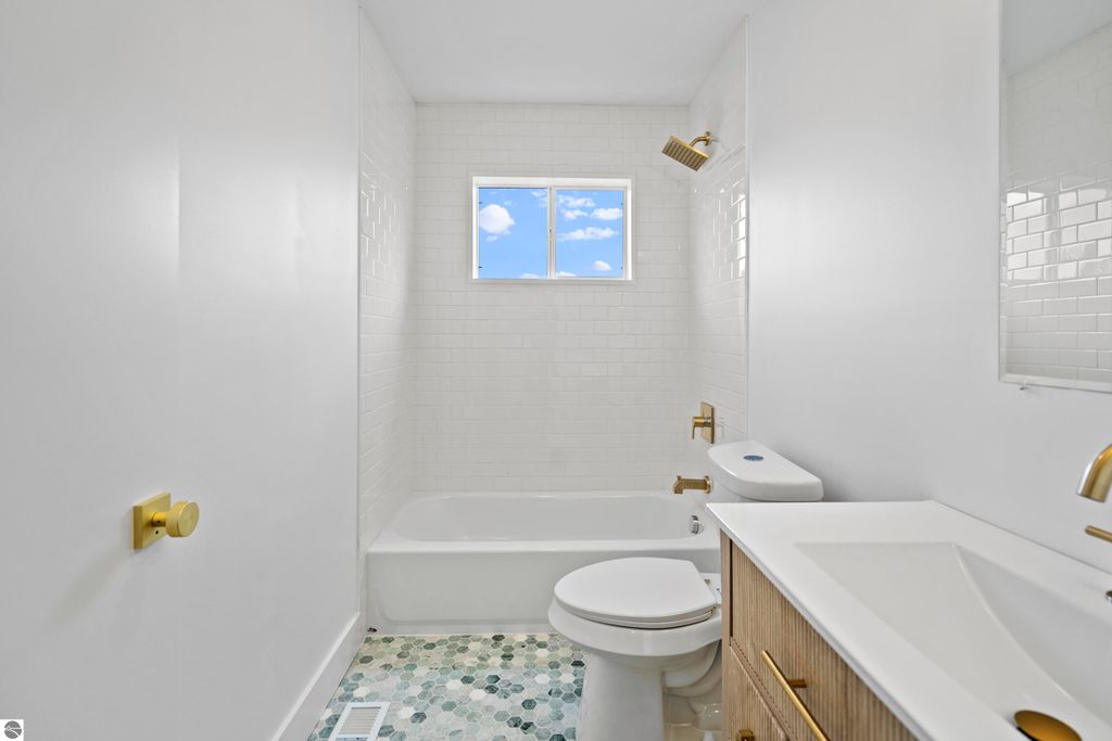 Bright, modern bathroom featuring a bathtub, gold fixtures, white subway tile, and a window with a view of blue sky, highlighting the home's contemporary design.
