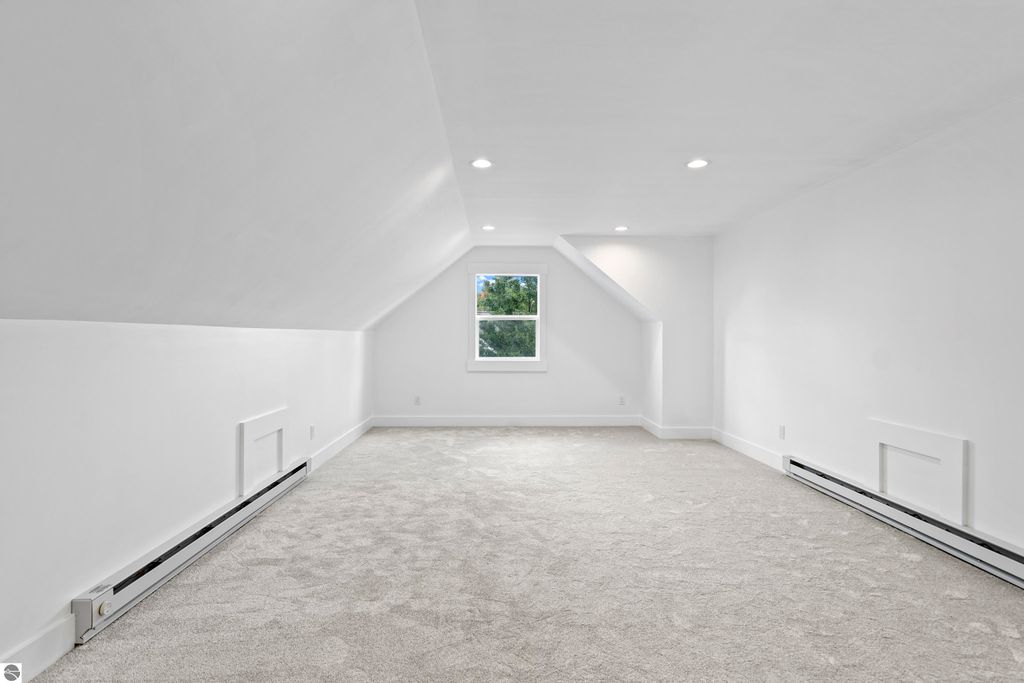 Bright, spacious upper-level room with sloped ceiling, large window, and plush carpet, ideal for versatile use in new home at 2737 Ruby Street, Traverse City.