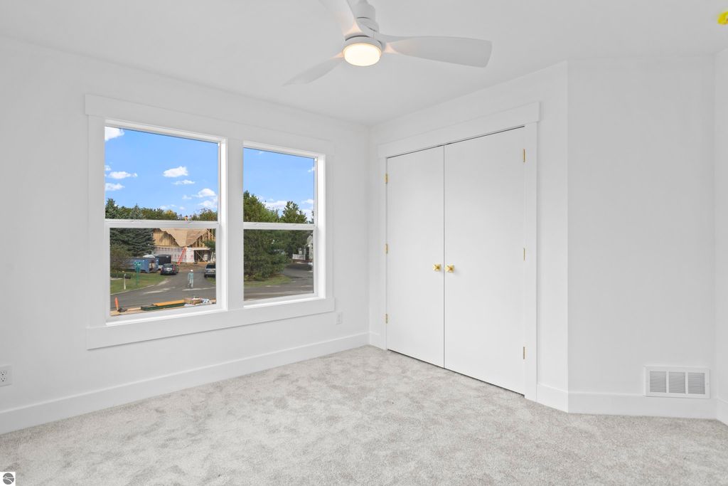 Bright, modern bedroom with large windows showcasing exterior views, plush carpet, and white closet doors, reflecting quality craftsmanship in a new home at 2737 Ruby Street, Traverse City, MI.