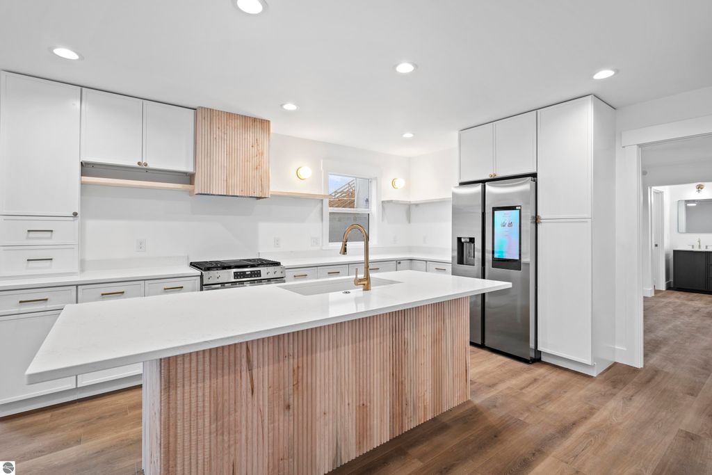 Modern kitchen featuring quartz countertops, custom cabinetry, energy-efficient stainless steel appliances, and a handcrafted vent hood, located in a new home in the Emerald Hills community of Traverse City, MI.