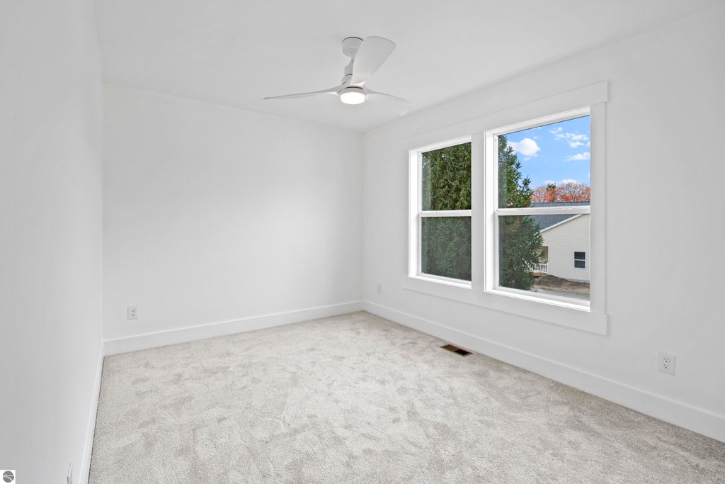 Bright, empty bedroom with plush carpet, modern ceiling fan, and large windows overlooking greenery, showcasing the spacious design of the new home at 2737 Ruby Street, Traverse City, MI.