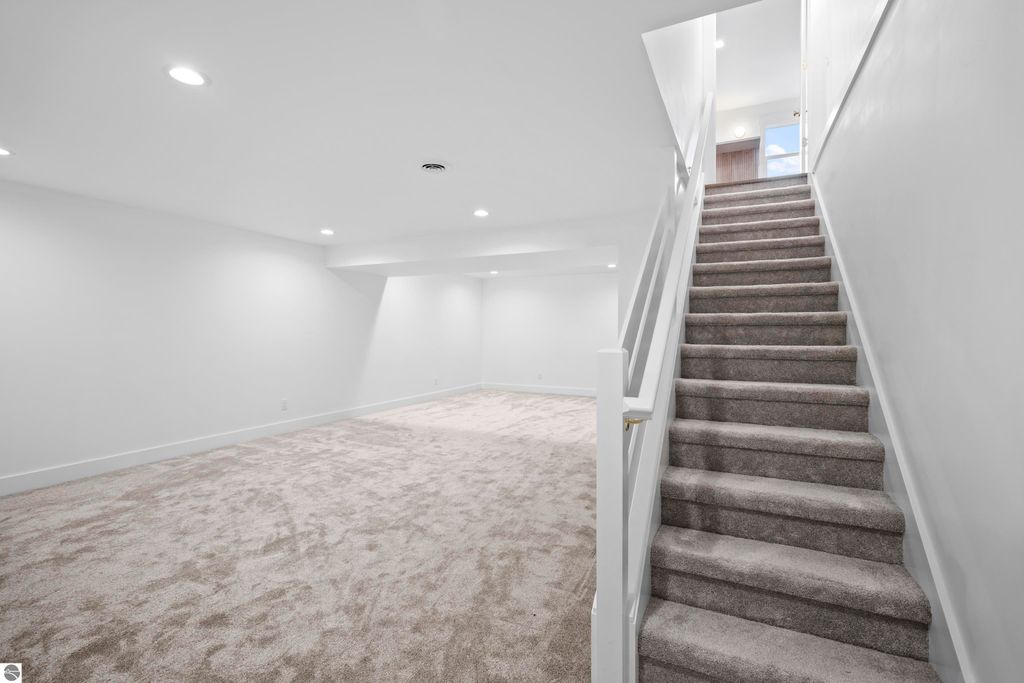 Spacious finished lower level with plush carpeting and bright lighting, featuring stairs leading to the main floor of a modern home in Traverse City, MI.
