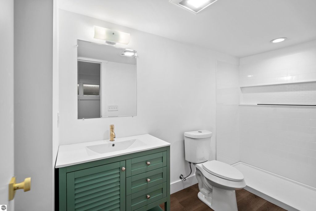 Modern bathroom featuring a green vanity with gold faucet, white countertop, large mirror, and tiled shower area, showcasing contemporary design elements in a new home in Traverse City.