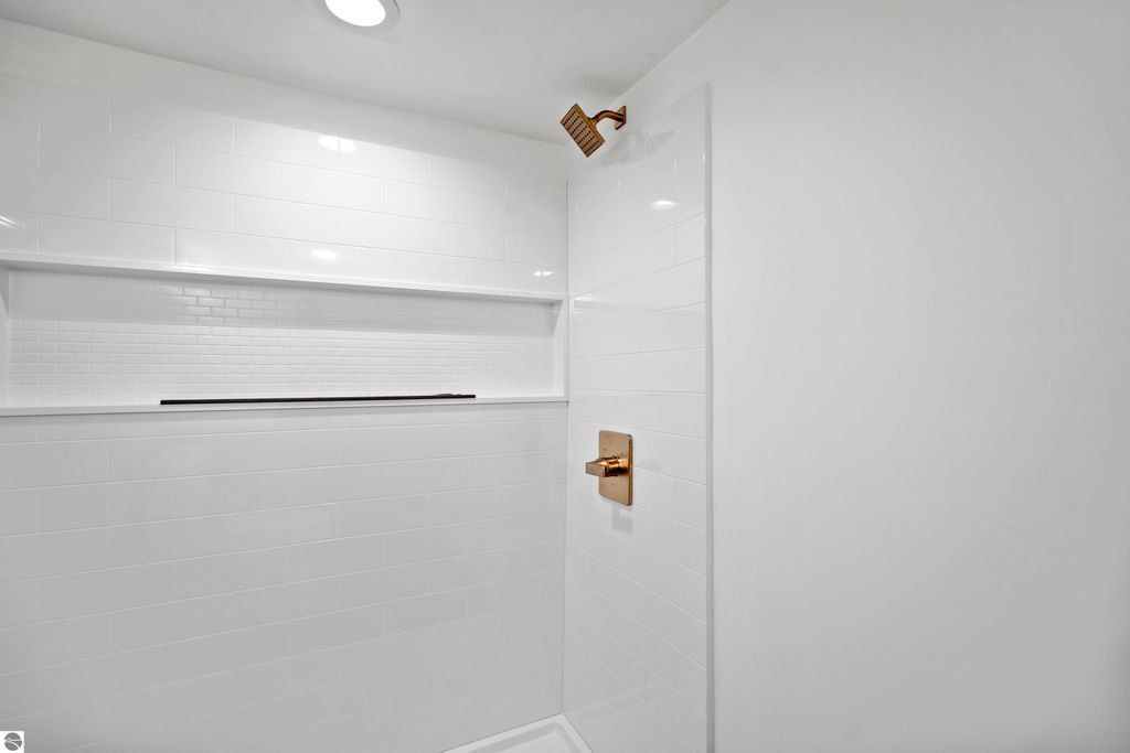 Modern bathroom shower with white subway tiles, bronze fixtures, and built-in shelf for storage.