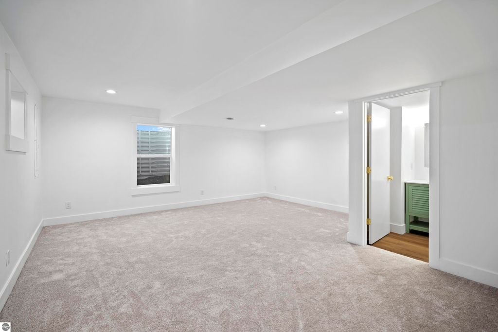Bright, spacious finished lower level with plush carpet, natural light from windows, and access to a bathroom area featuring a green vanity, ideal for versatile use in the Traverse City home listing at 2737 Ruby Street.