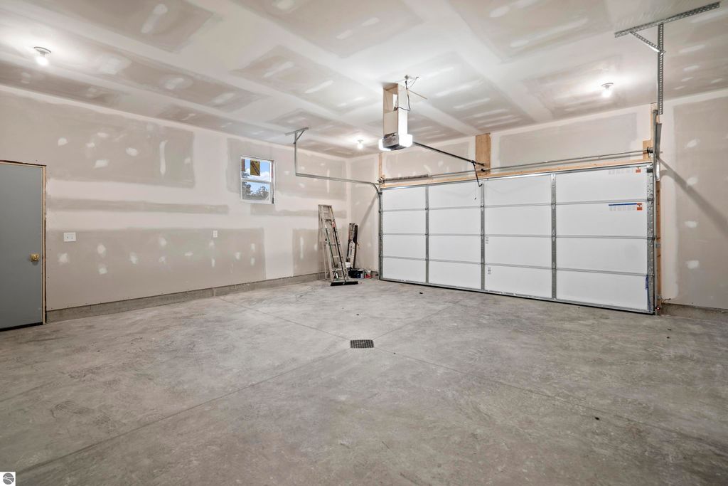 Spacious unfinished garage with drywall, concrete floor, and overhead lighting, part of the new home at 2737 Ruby Street, Traverse City, MI.