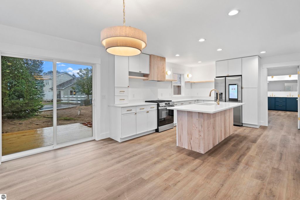 Modern kitchen featuring white cabinetry, quartz countertops, and stainless steel appliances, with a view of the outdoors through sliding glass doors, showcasing craftsmanship in the new Traverse City home at 2737 Ruby Street.