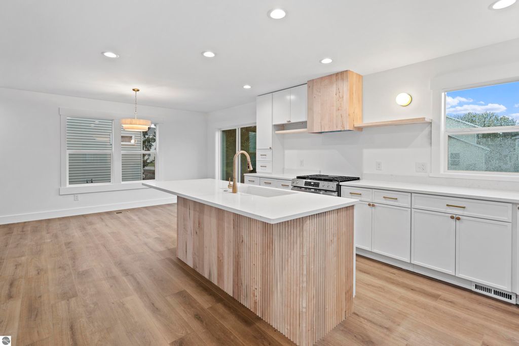Modern kitchen with quartz countertops, custom cabinetry, and open shelving, featuring a central island with wood detailing, energy-efficient appliances, and large windows providing natural light, located in a new home at 2737 Ruby Street, Traverse City, MI.