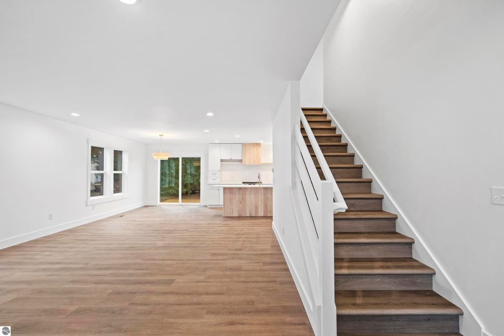 Bright, open living area showcasing modern design elements, featuring hardwood floors, large windows, and a staircase leading to upper levels, with a view of a custom kitchen equipped with energy-efficient appliances and quartz countertops.