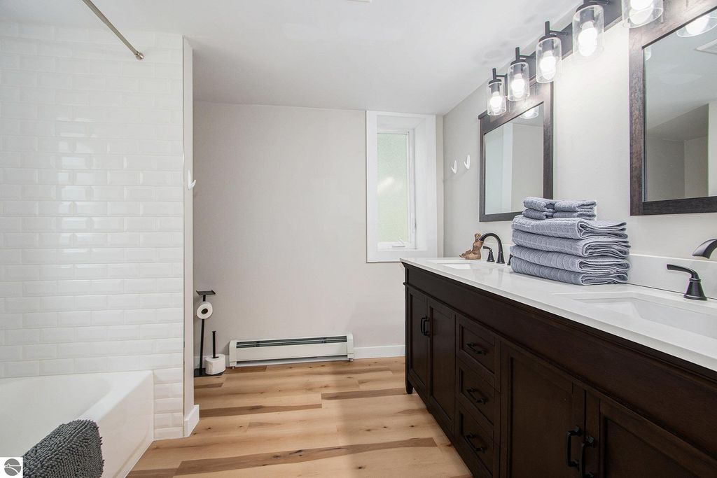Modern bathroom featuring double sinks, dark wood cabinetry, and stacked towels, with white subway tile and natural wood flooring.