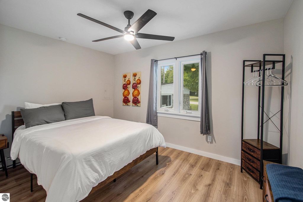 Renovated bedroom in Onekama, MI featuring a queen bed, decorative wall art, window with natural light, and modern furnishings, ideal for rental opportunities near Portage Lake.