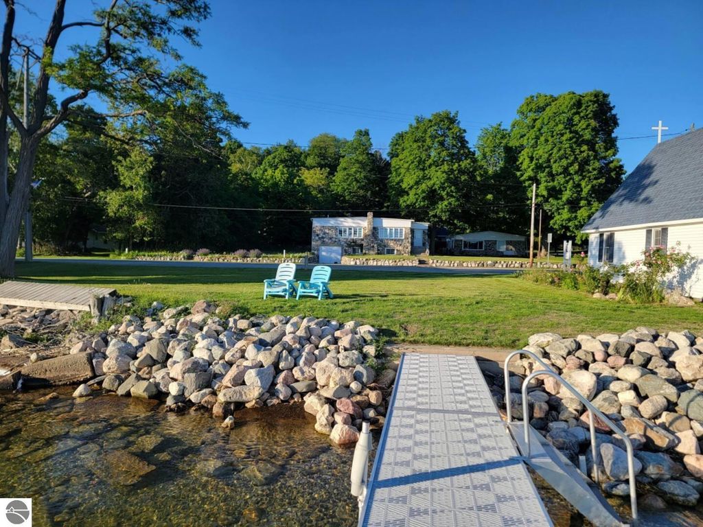 Scenic view of stone cottages at 4642 Main Street, Onekama, MI, featuring a dock, lawn, and Adirondack chairs by Portage Lake, ideal for vacation rentals.