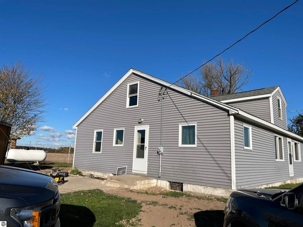 Four-bedroom farmhouse at 6034 W Sterling Road, Sterling, MI, featuring a gray exterior, large yard, and open views of surrounding farmland, set on 2.5 acres.