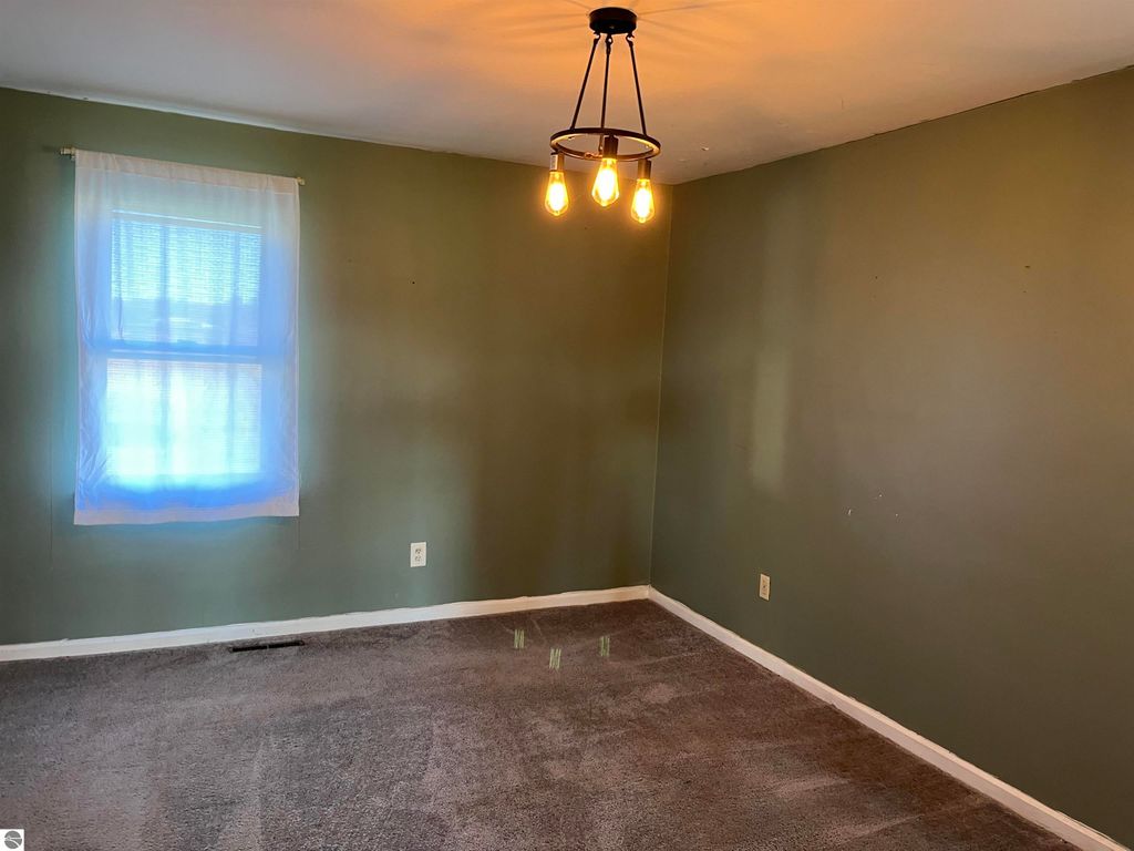 Interior view of a four-bedroom farmhouse for sale at 6034 W Sterling Road, featuring green walls, a window with sheer curtains, and a modern light fixture, highlighting the property's potential for renovation and personalization.