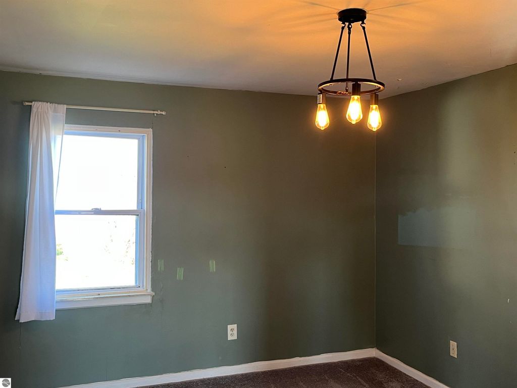 Interior view of a room in a farmhouse at 6034 W Sterling Road, featuring a window with white curtains, green walls, and a modern light fixture with exposed bulbs, highlighting the need for renovation and potential for personalization.