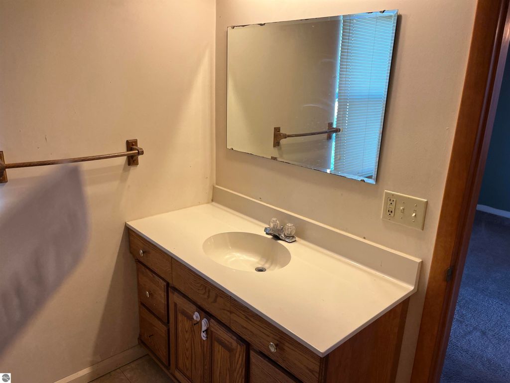 Bathroom vanity with sink, mirror, and wooden cabinetry, showcasing a simple design in a four-bedroom farmhouse for sale in Sterling, MI.