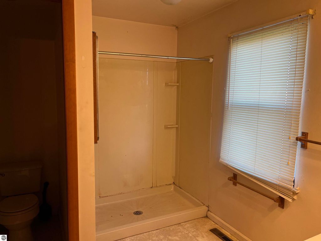 Bathroom interior featuring a shower stall, toilet, and window with blinds, highlighting potential for renovation in the farmhouse at 6034 W Sterling Road, Sterling, MI.