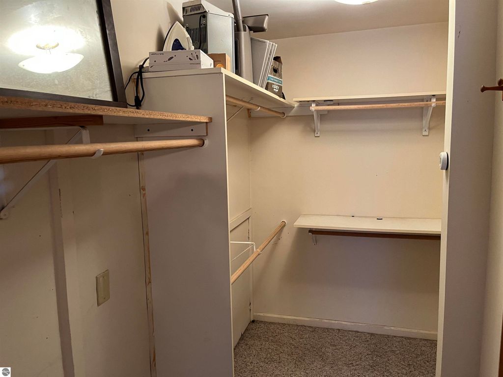 Interior view of a spacious closet in a four-bedroom farmhouse, featuring wooden shelves, a hanging rod, and carpeted flooring, highlighting storage potential in the property at 6034 W Sterling Road, Sterling, MI.