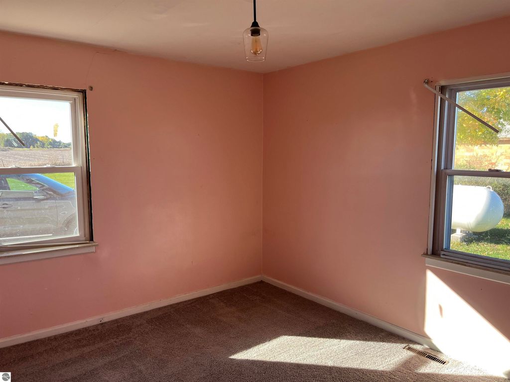 Interior view of a four-bedroom farmhouse in Sterling, MI, featuring pink walls, carpeted floor, and windows allowing natural light, showcasing potential for renovation and personalization.