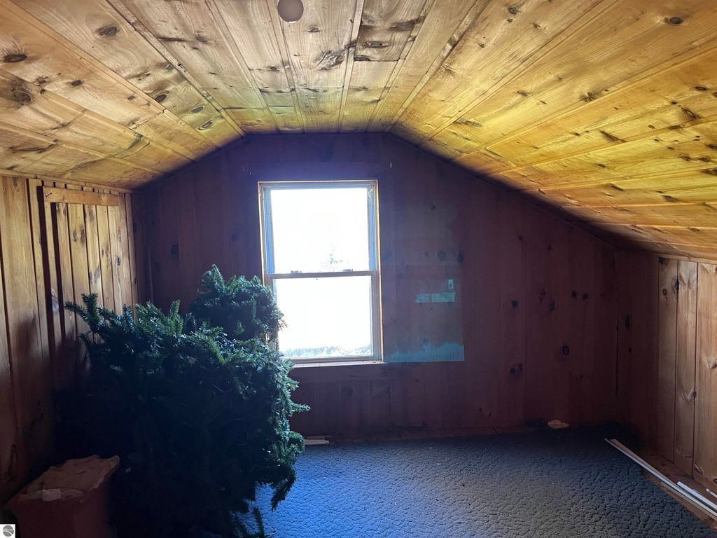 Attic room with wooden walls, a window providing natural light, and a partially decorated artificial Christmas tree, reflecting the rustic charm of the farmhouse at 6034 W Sterling Road, Sterling, MI.