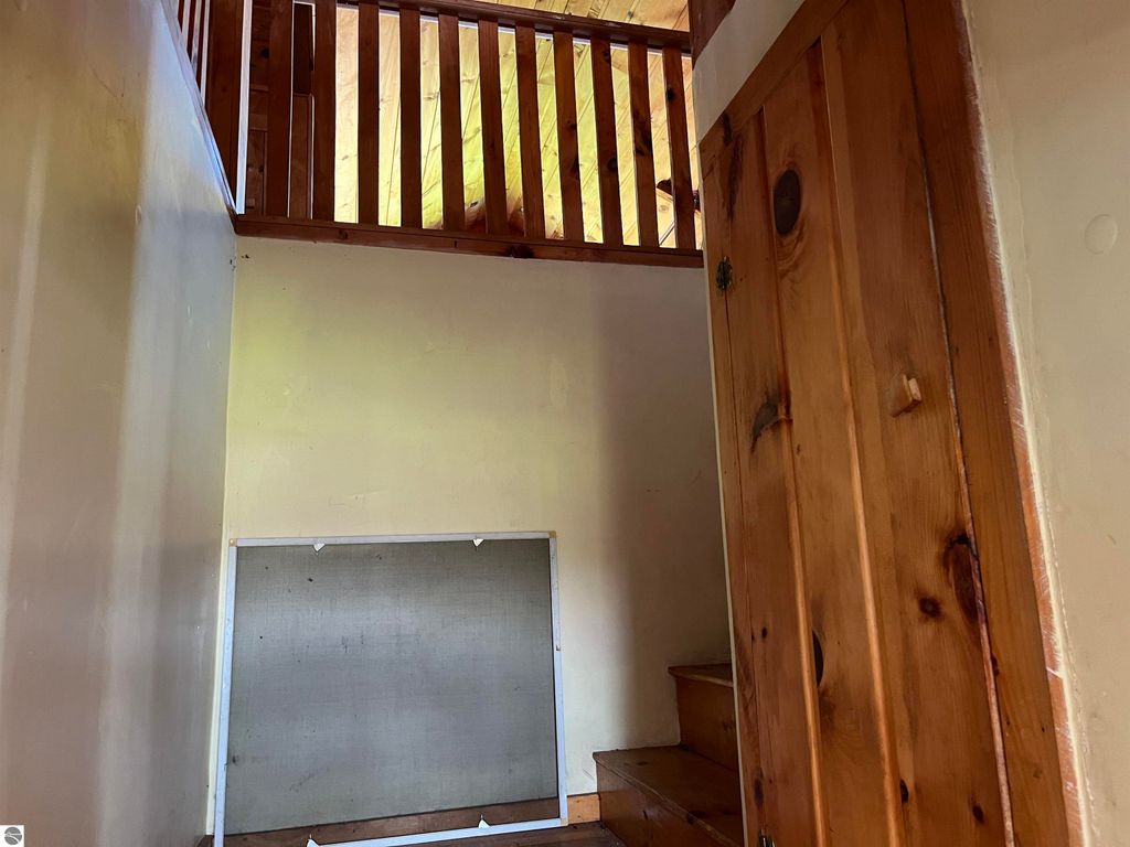 Staircase leading to upper level of a four-bedroom farmhouse at 6034 W Sterling Road, showcasing wooden railings and a rustic door, reflecting rural charm.