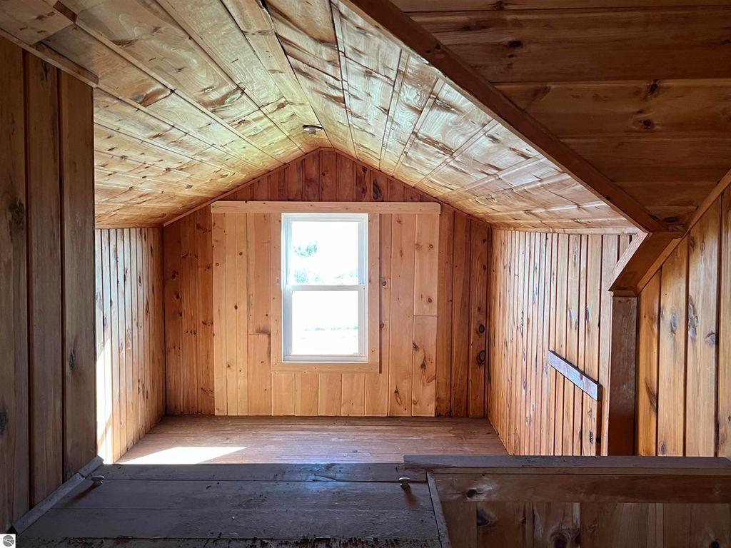 Interior view of a rustic wooden loft space with a window, showcasing natural wood paneling and beams, part of a four-bedroom farmhouse for sale on 2.5 acres in Sterling, MI.