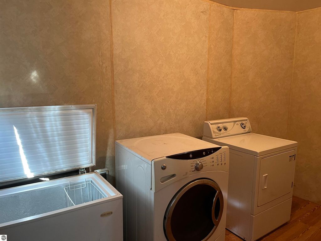 Laundry room featuring a front-loading washer, a dryer, and a chest freezer against a textured wall, highlighting the home's utility space in the real estate listing for 6034 W Sterling Road, Sterling, MI.