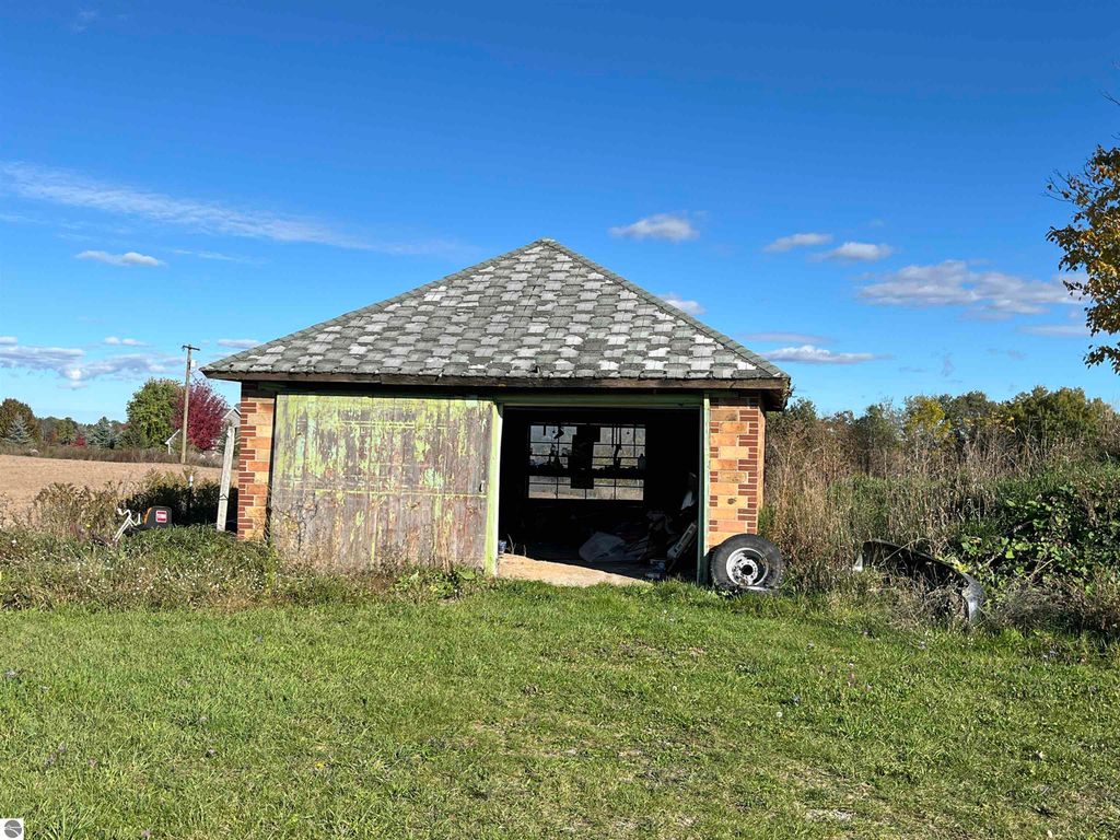 Outbuilding with a weathered green door and a shingled roof, situated on a rural property in Sterling, MI, surrounded by grass and open farmland.