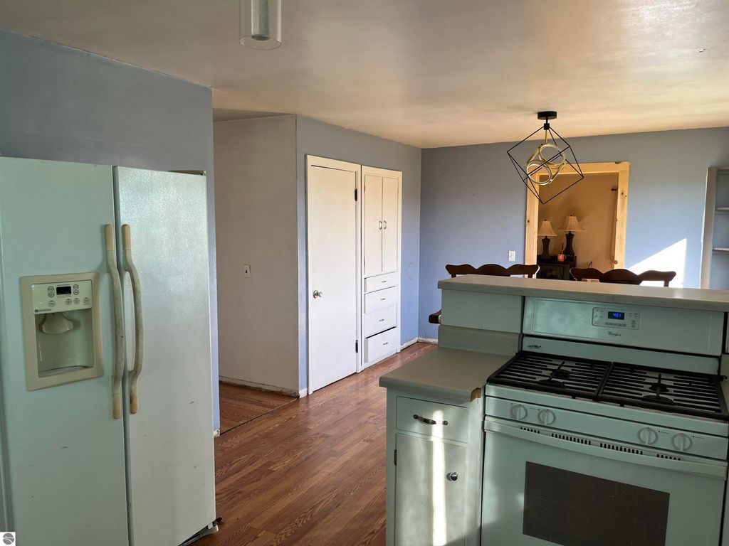 Interior view of a kitchen featuring a white refrigerator, gas stove, wooden cabinets, and an open layout, highlighting the farmhouse style of the property at 6034 W Sterling Road, Sterling, MI.