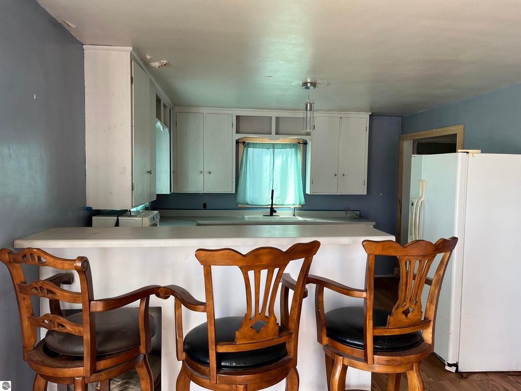 Interior view of a farmhouse kitchen featuring a white countertop, wooden bar stools, light blue walls, and cabinets, with a window showcasing natural light.