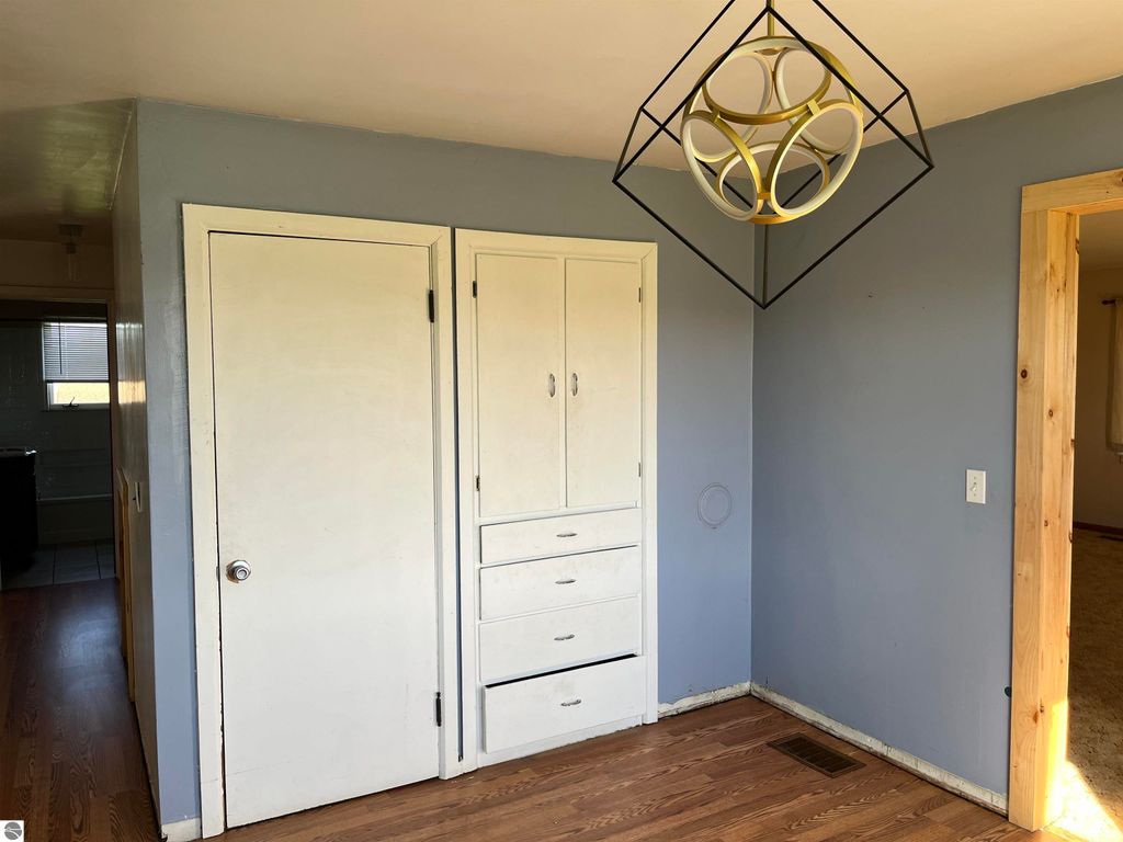 Interior view of a farmhouse entryway featuring a closet with drawers, a light fixture, and hardwood flooring, showcasing the property's potential for rural living at 6034 W Sterling Road, Sterling, MI.