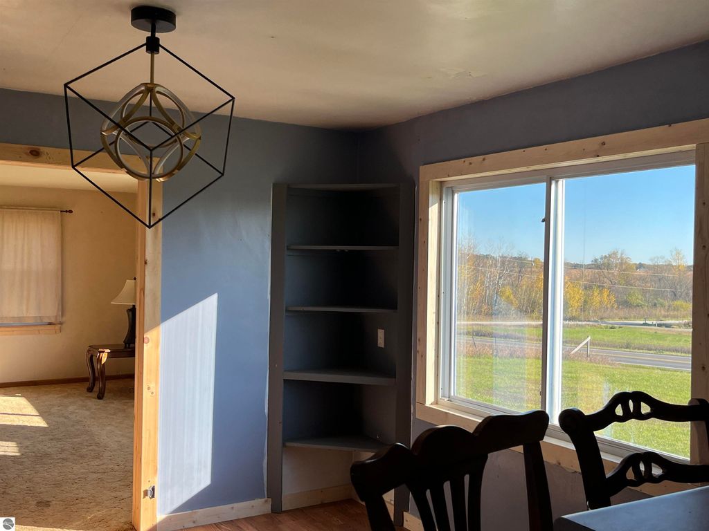 Interior view of a farmhouse featuring a modern geometric light fixture, a window with rural views, and a built-in shelf, highlighting the home's potential for country living at 6034 W Sterling Road, Sterling, MI.