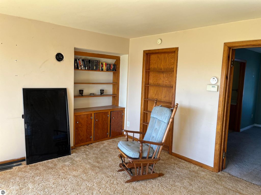 Living room interior of a farmhouse with a rocking chair, wooden shelving, and a flat-screen TV, showcasing a cozy rural atmosphere in Sterling, MI.