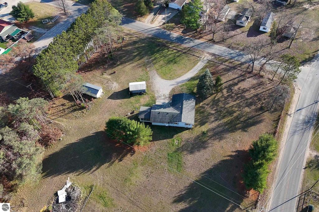 Aerial view of a single-family home at 2265 Michigan Avenue, Prescott, MI, surrounded by a large yard, trees, and outbuildings, highlighting the property's 3-acre lot and serene setting near Bush Lake and Skidway Lake.