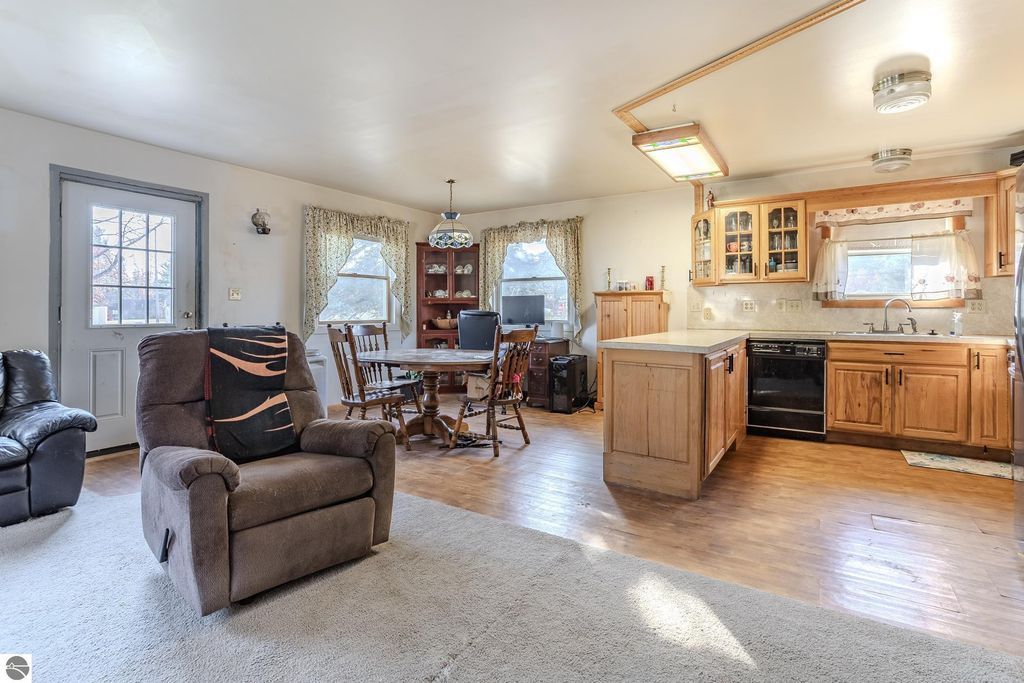 Cozy interior of a 2-bedroom home in Prescott, MI, featuring a living area with a recliner, dining table, and kitchen with wooden cabinets, ideal for a serene lifestyle.