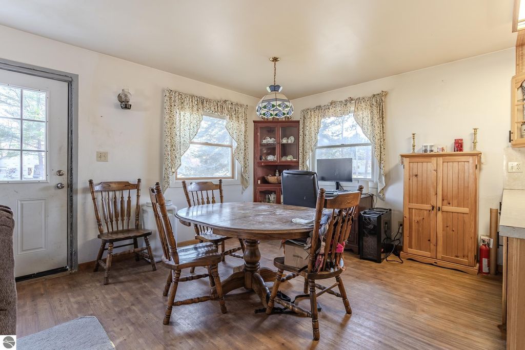 Dining area in Prescott, MI home featuring a round wooden table, four wooden chairs, and a view of the outdoors through two windows, with a cozy atmosphere enhanced by natural light and decorative elements.