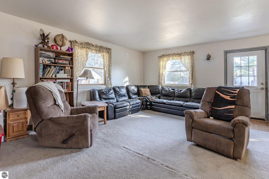 Living room of a home at 2265 Michigan Avenue, Prescott, MI, featuring a large black sectional sofa, a cozy recliner, bookshelves, and bright windows, highlighting a comfortable and inviting space ideal for relaxation.