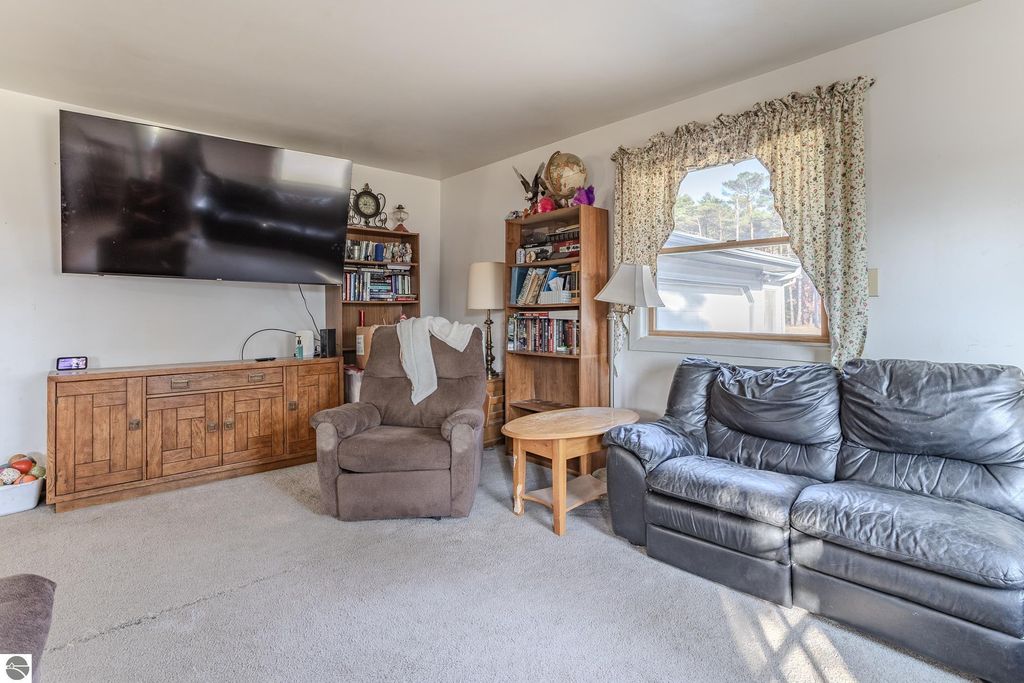 Living room interior of a home at 2265 Michigan Avenue, featuring a large flat-screen TV, wooden furniture, a cozy armchair, and a bookshelf, with natural light streaming through a window.