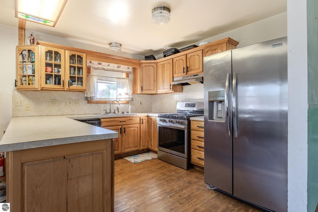 Kitchen interior featuring wooden cabinets, stainless steel refrigerator, gas stove, and sink, showcasing the functional layout of the home at 2265 Michigan Avenue, Prescott, MI.